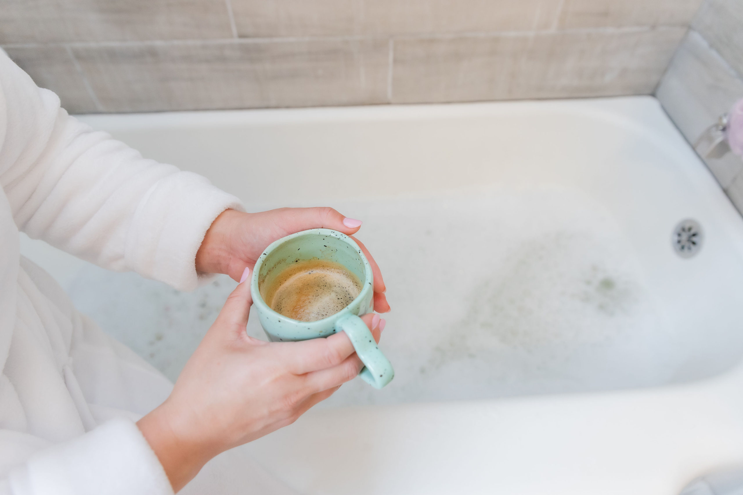 white-lady-hand-holding-a-cup-of-cofee-over-a-bath-tub-bubble-bath-setting