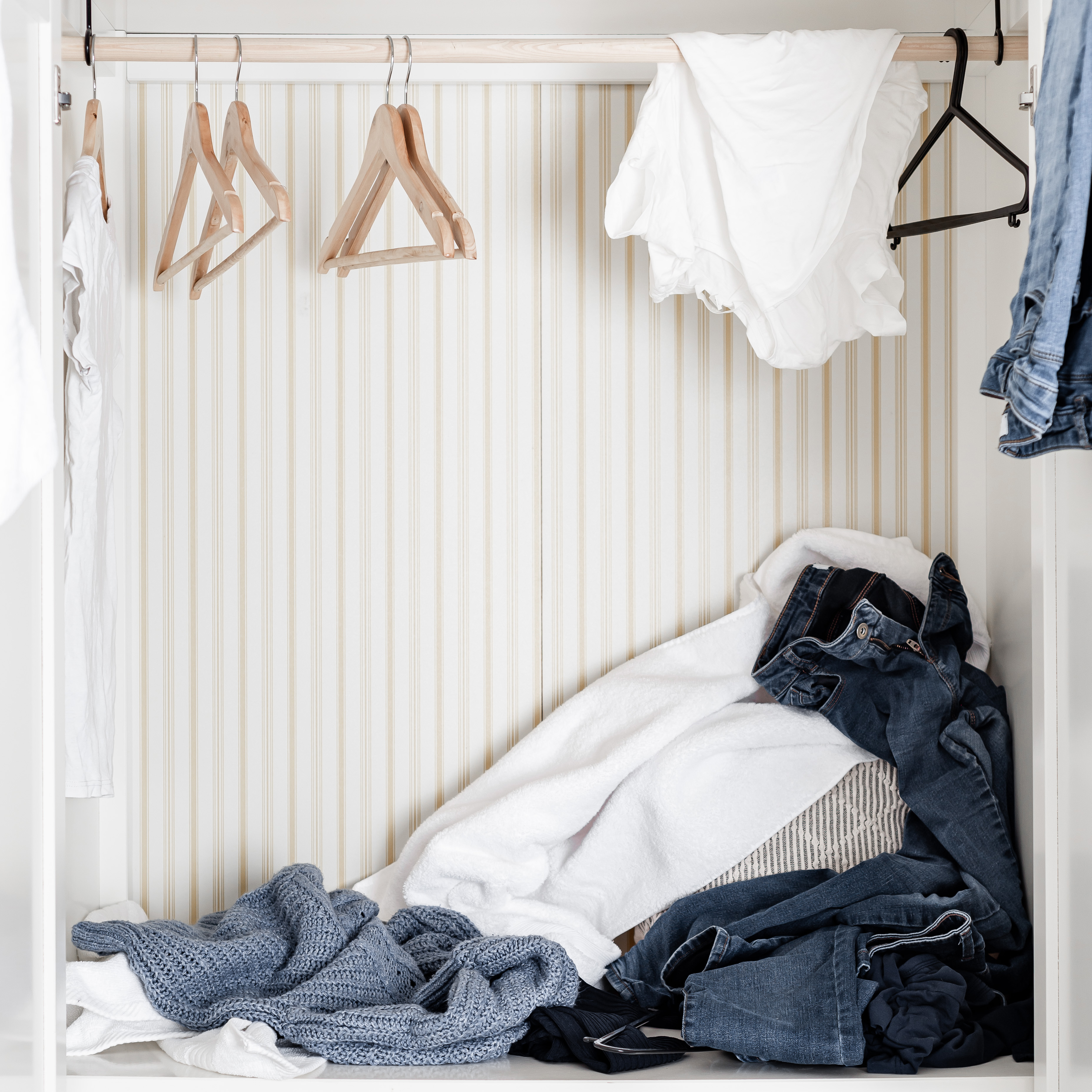 brown-wooden-hangers-in-a-wardrobe-with-white-and-blue-clothes-scattered-down