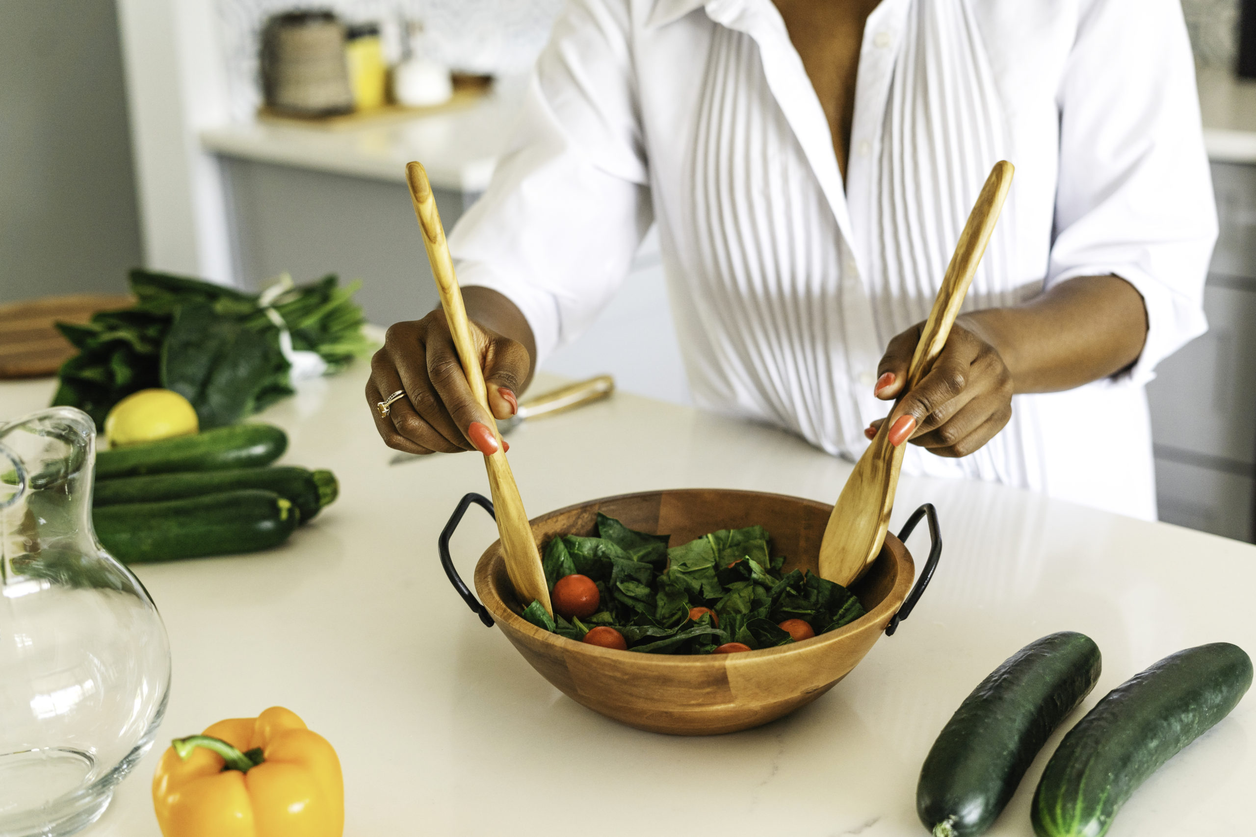 black-lady-wearing-a-white-shirt-and-mixing-greenish-food-in-a-wooden-bowl-on-a-cream-colour-table-top