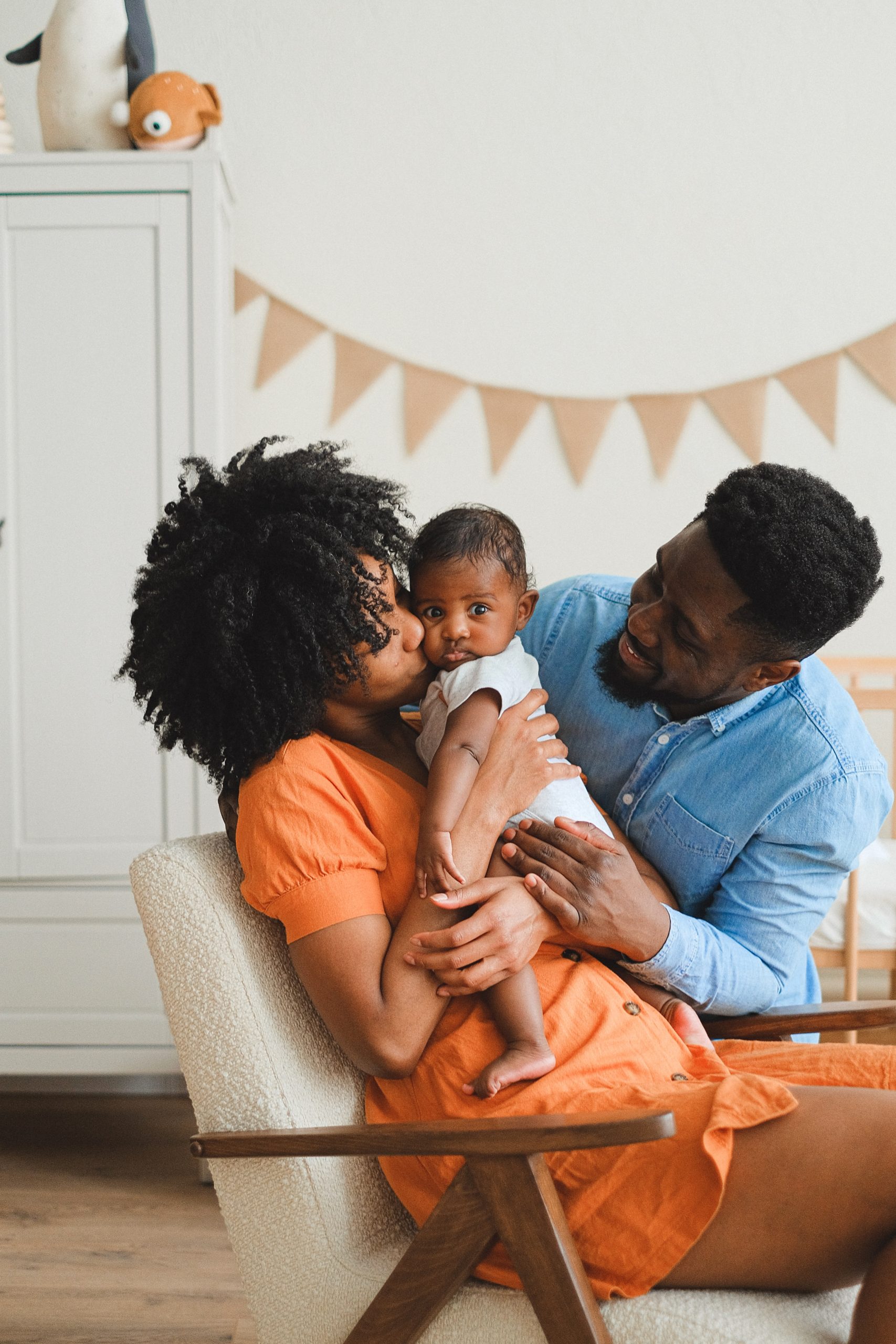black-woman-wearing-an-orange-dress-sitting-on-a-chair-with-a-black-baby-and-her-husband