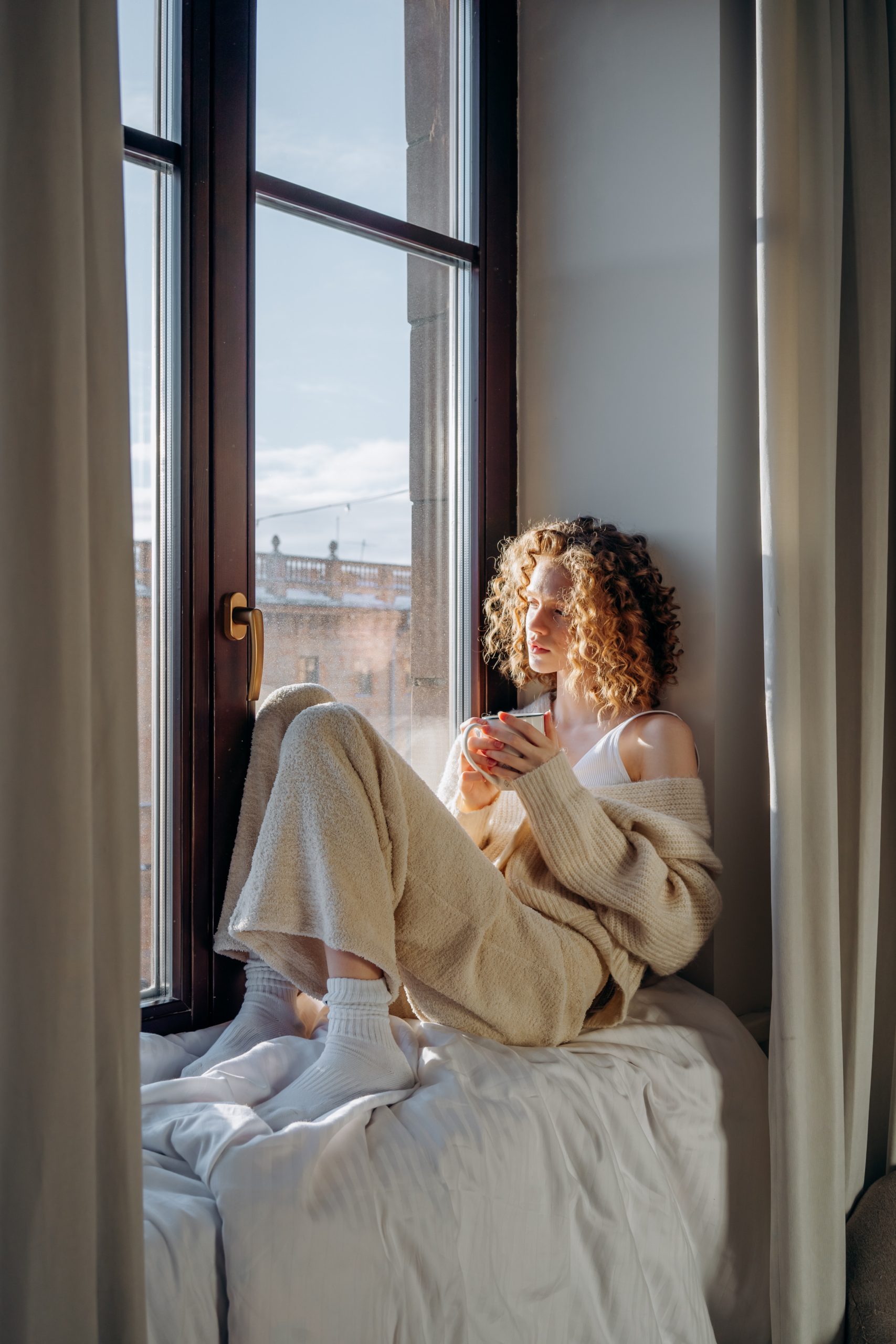 blone-curly-hair-lady-sitting-beside-the-window-with-a-cup-of-cofee-in-deep-thoughts