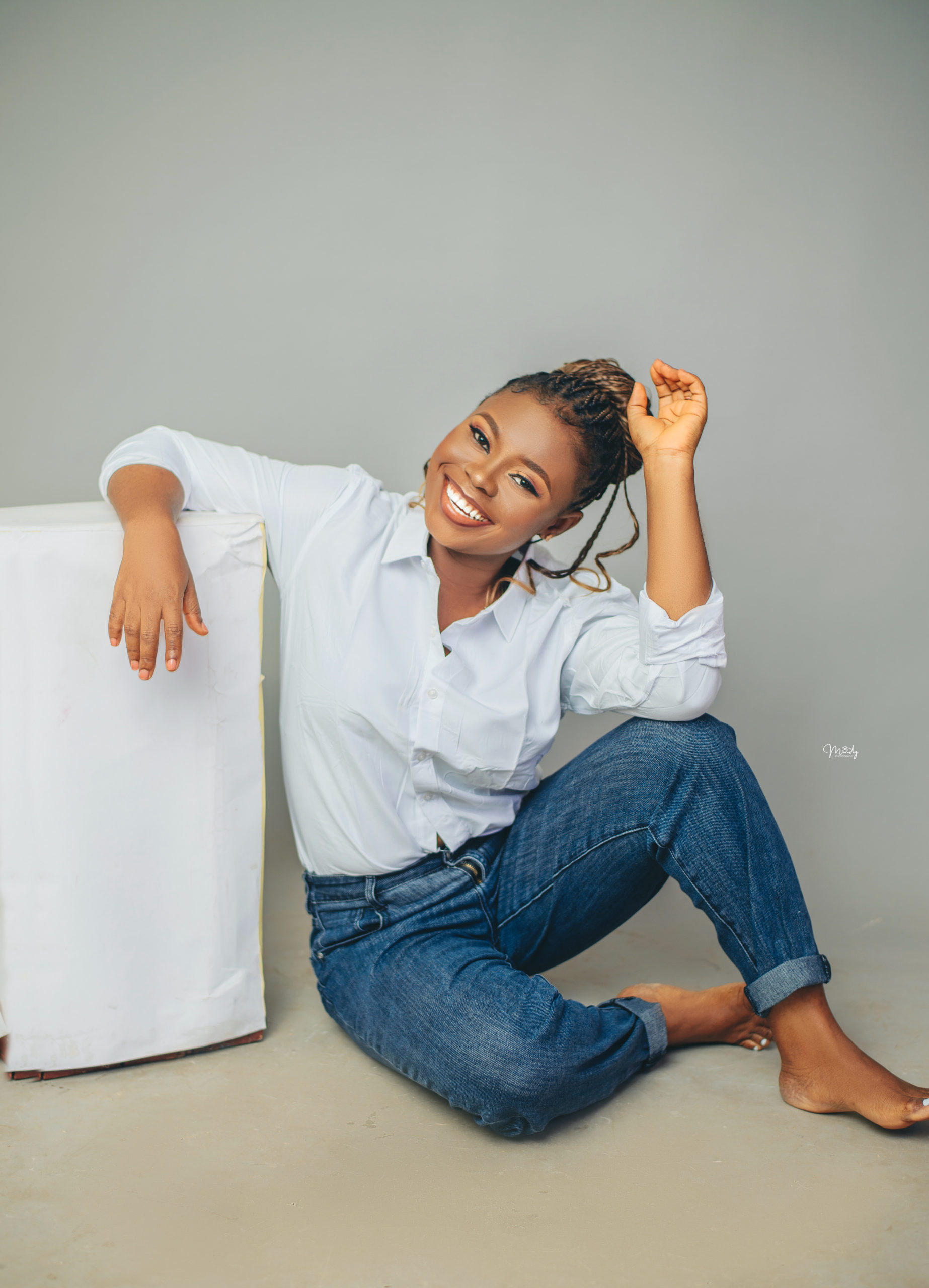 Joy-Onovo-wearin- a-white-shirt-and-blue-jean-sitting-on-the-floor-legs-crossed-and-smiling-broadly