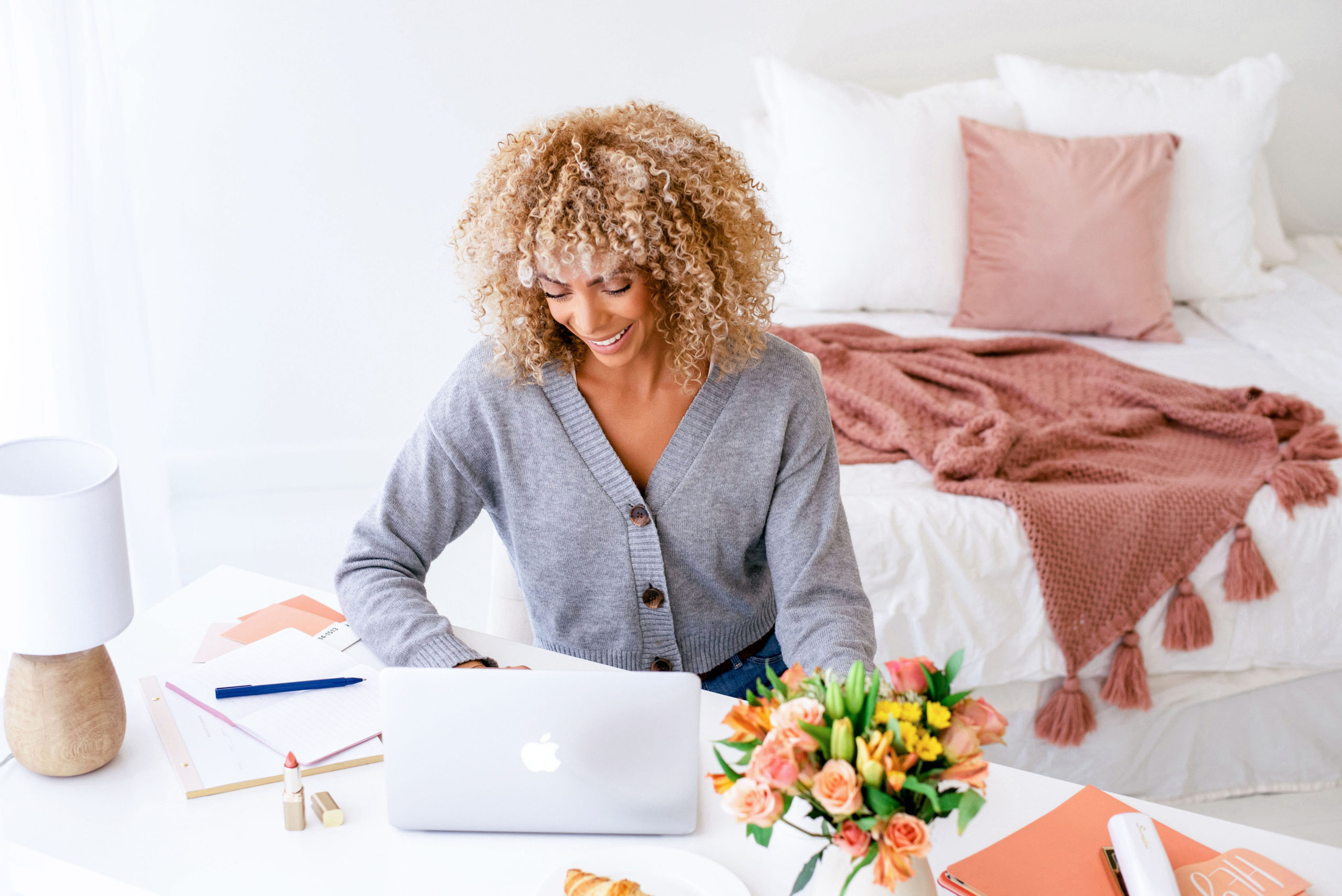 black-woman-with-blonde-curly-hair-wearing-a-blue-top-and-looking-at-a-laptop-on-a-white-table