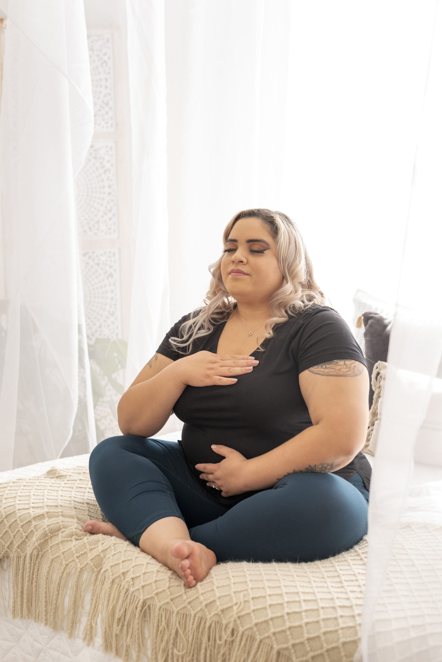 plus-size-woman-wearing-a-black-top-and-a-blue-denim-pant-sitting-on-a-bed-with-legs-crossed