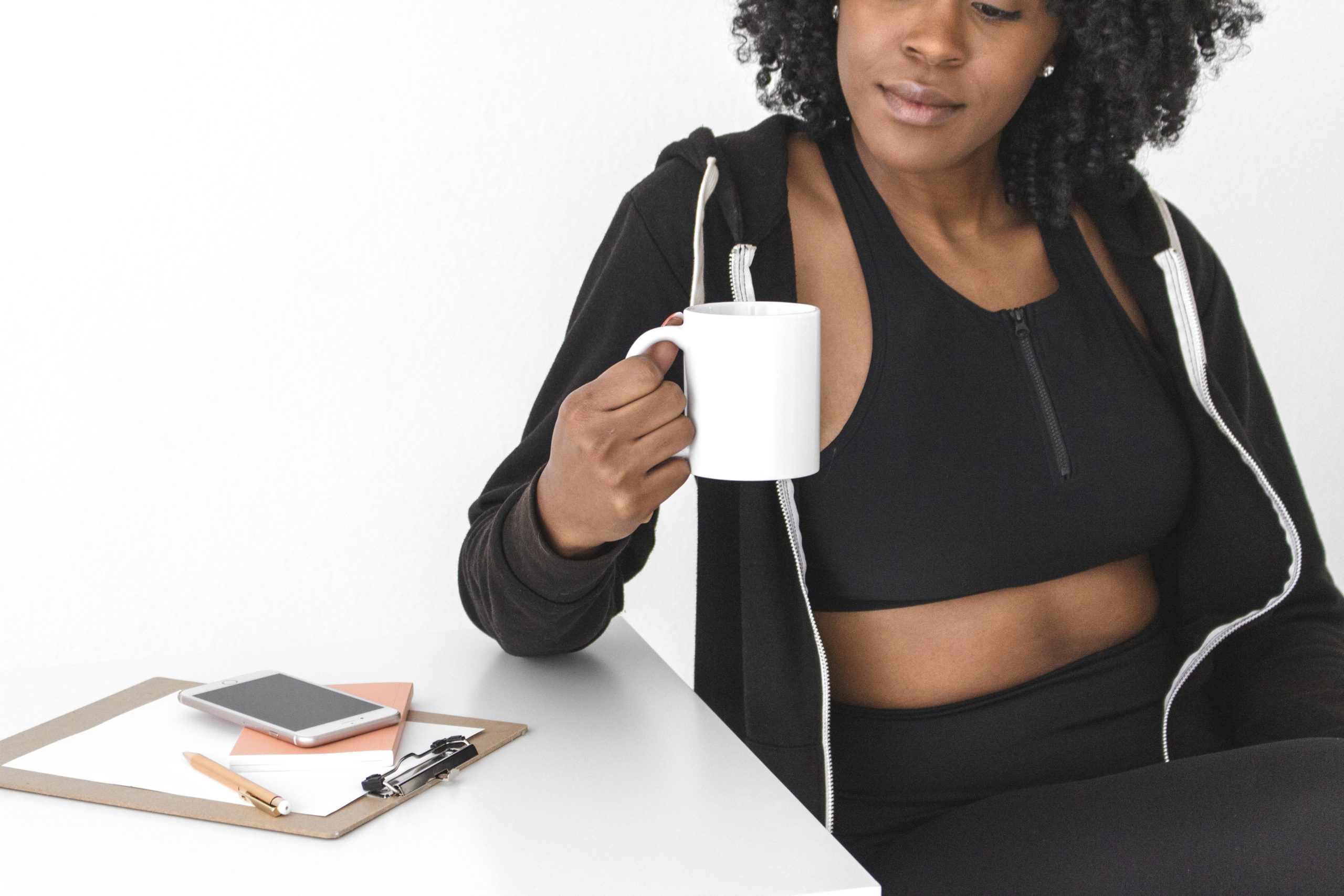 black-lady-with-curly-hair-in-a-black-work-out-outfit-holding-a-white-cup-of-drink-sitting-down