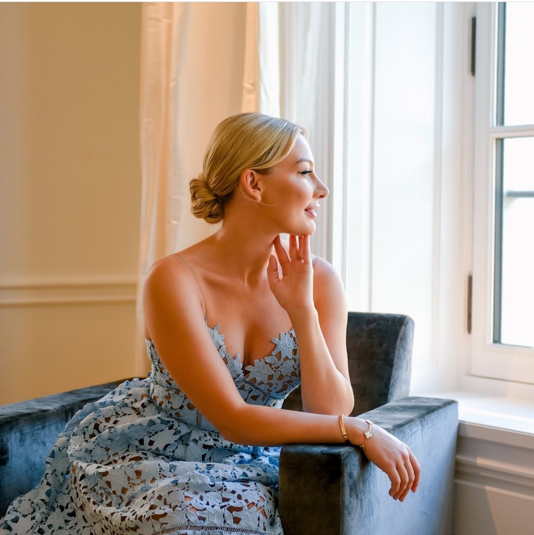 anna bey wearing a blue flowery dress and looking out the window