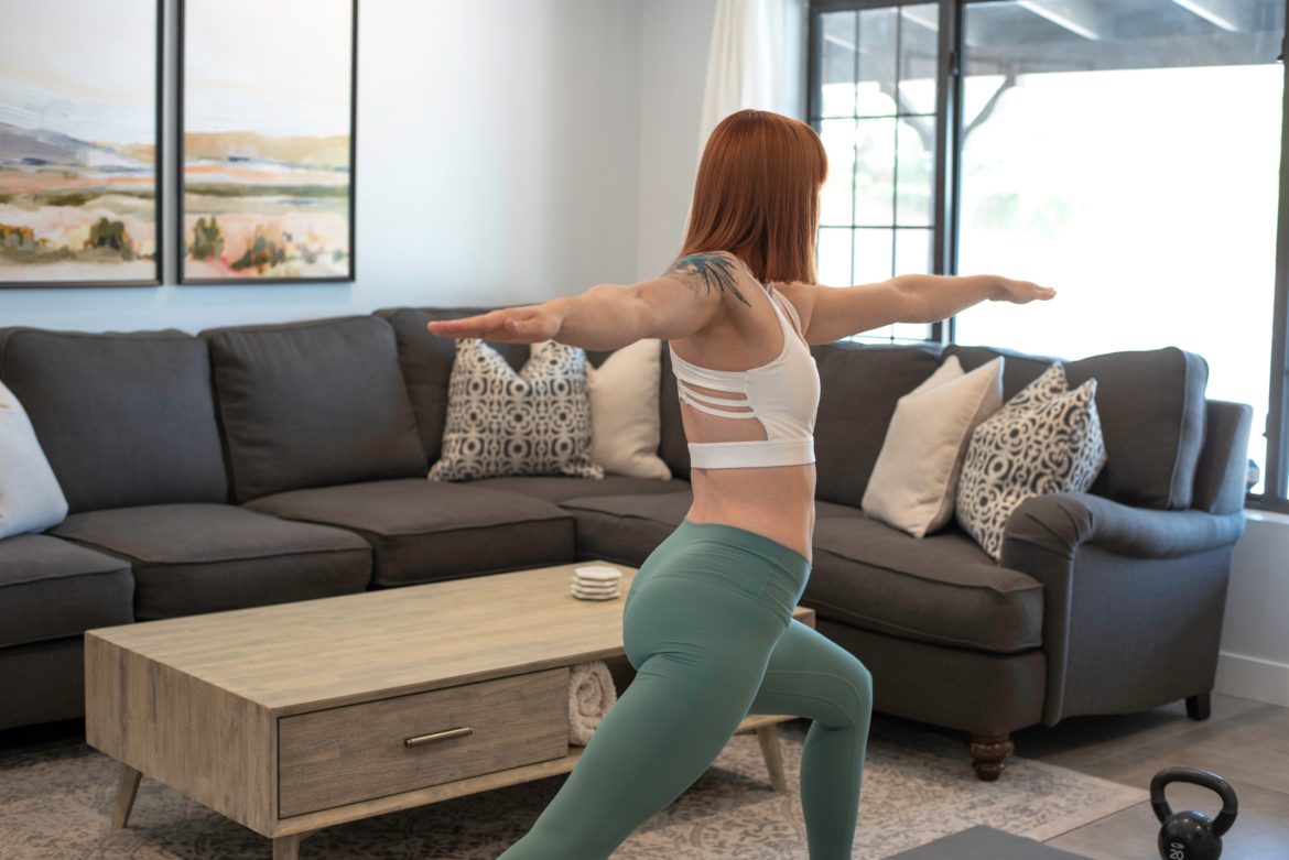 white-red-haired-lady-wearing-a-white-bra-top-and-a-green-pants-stretching-in-her-sitting-room