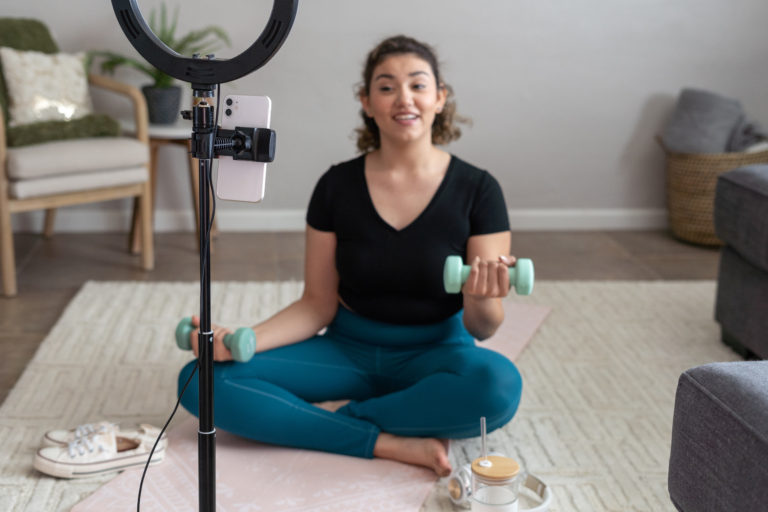 whie-lady-wearing-a-black-top-and-blue-denim-pant-sitting-legs-crossed-on-the-floor-in-front-of-a-ringlight-filming