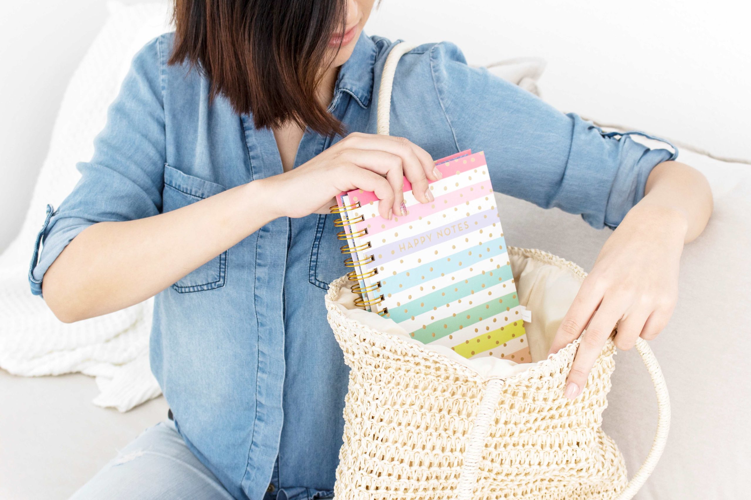 white lady wearing a sky blue denim shirt and putting a colourful book in her brown knitted hand bag