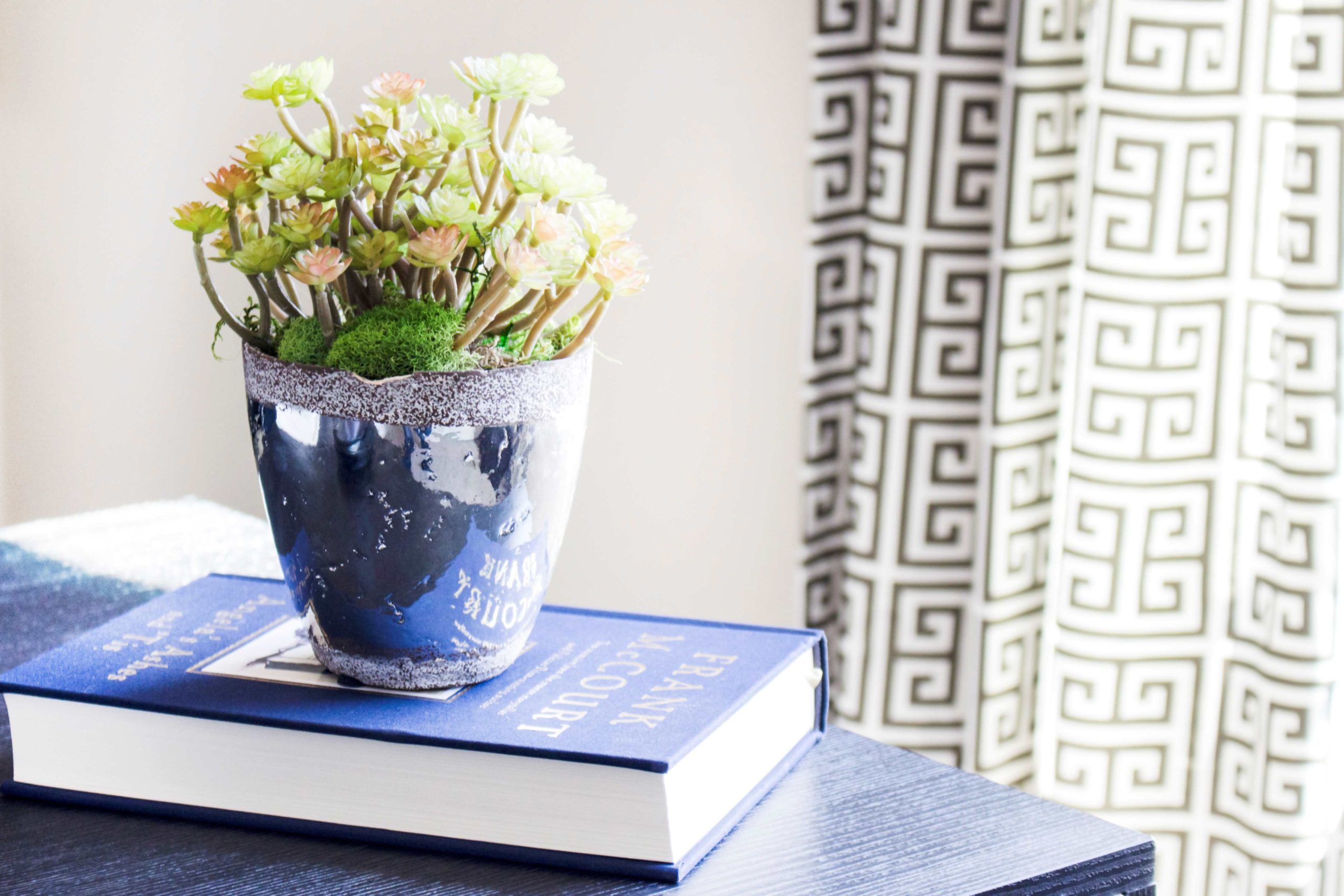 green and white flowers in a blue glass vase on a blue book on a blue desk