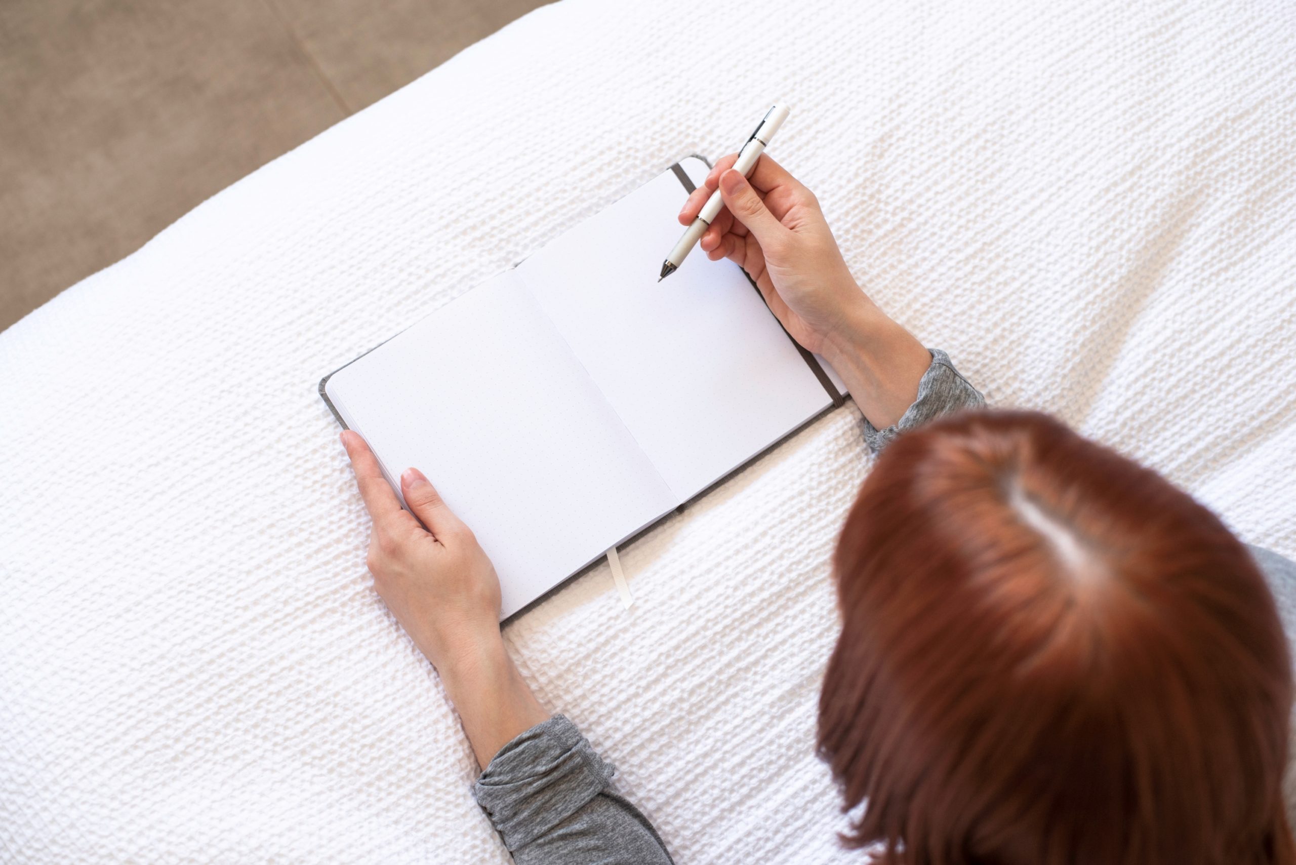 white red hair lady practicing journaling while lying down on a white bed