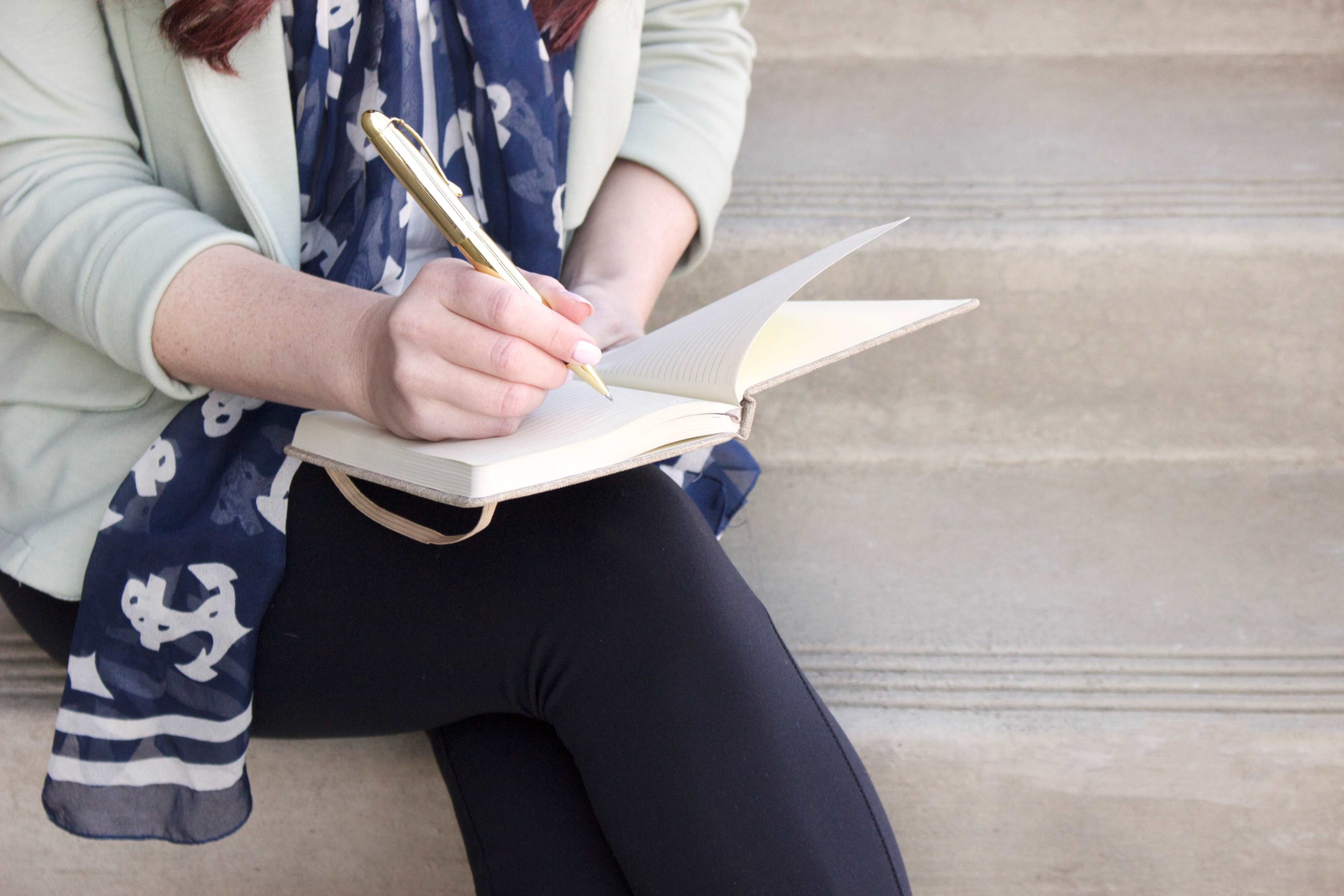 white lady sitting outdoors on a step journaling