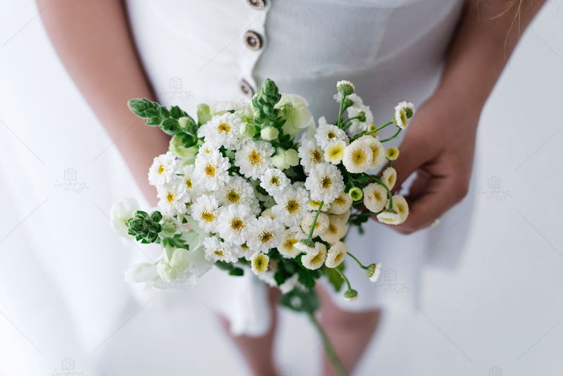 woman wearing a white button down dress and holding a white and green coloured flower