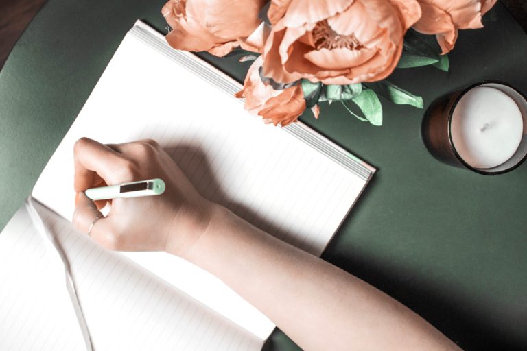 white lady hand writing on a blank journal on a green table