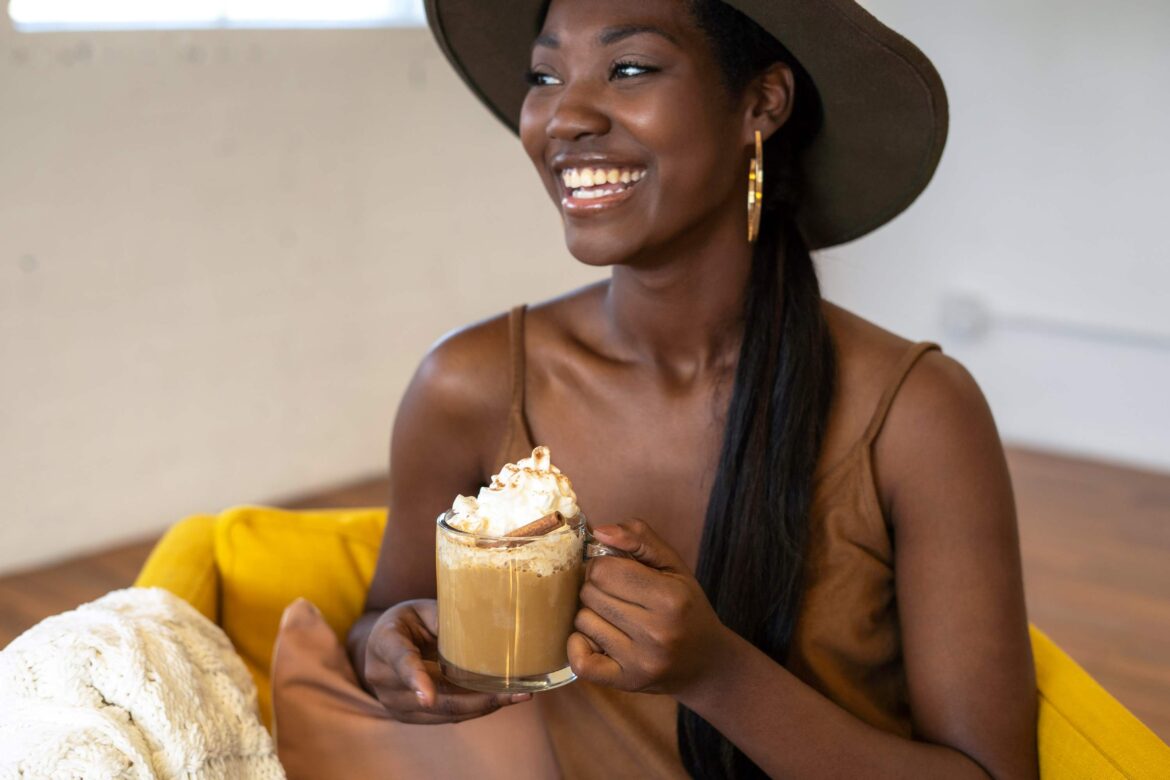 black-lady-wearing-a-brown-fedora-hat-smiling-with-a-cup-of-drink-looking-unbothered